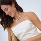 Model wearing a white strapless dress with a south sea pearl necklace and south sea pearl hoop earrings against a light background