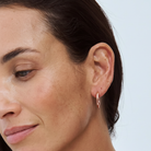 Close-up of an ear wearing a 9k yellow gold hoop earring on a light background