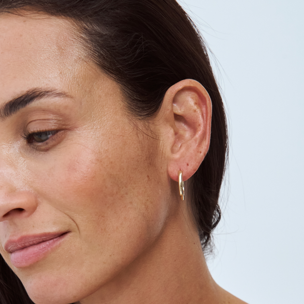 Close-up of an ear wearing a 9k yellow gold hoop earring on a light background