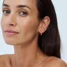 Close-up of a model wearing a small, solid gold hoop earring.