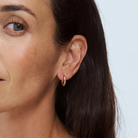 Close-up of a woman wearing a 9k rose gold hoop earring against a light background