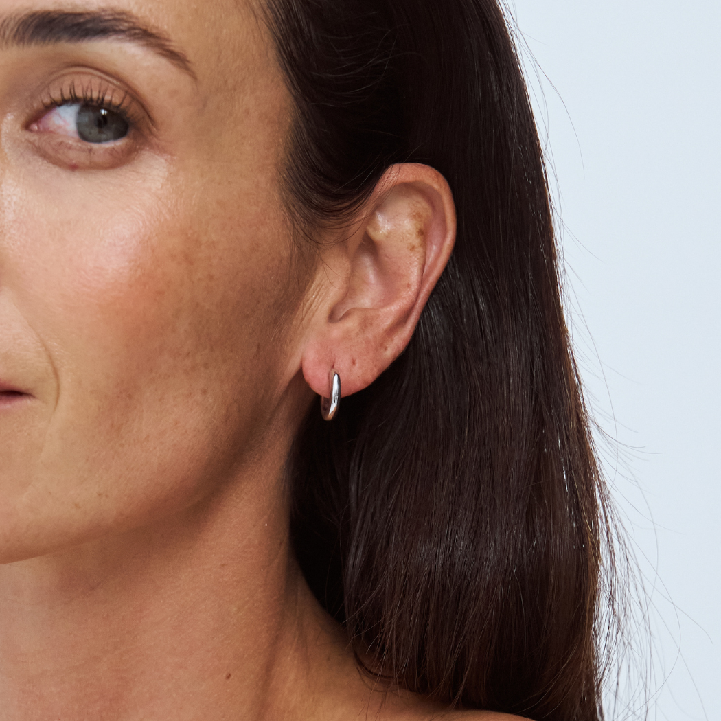 Close-up of a woman's ear with a 9k white gold earring against a light background