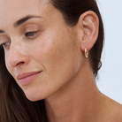 Close-up of a woman wearing a 9k yellow gold hoop earring against a light background