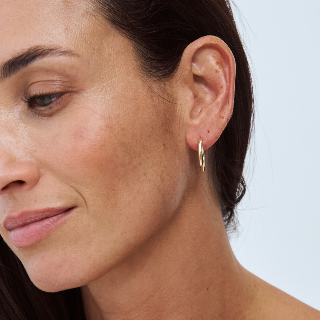 Close-up of a woman wearing a 9k yellow gold hoop earring against a light background