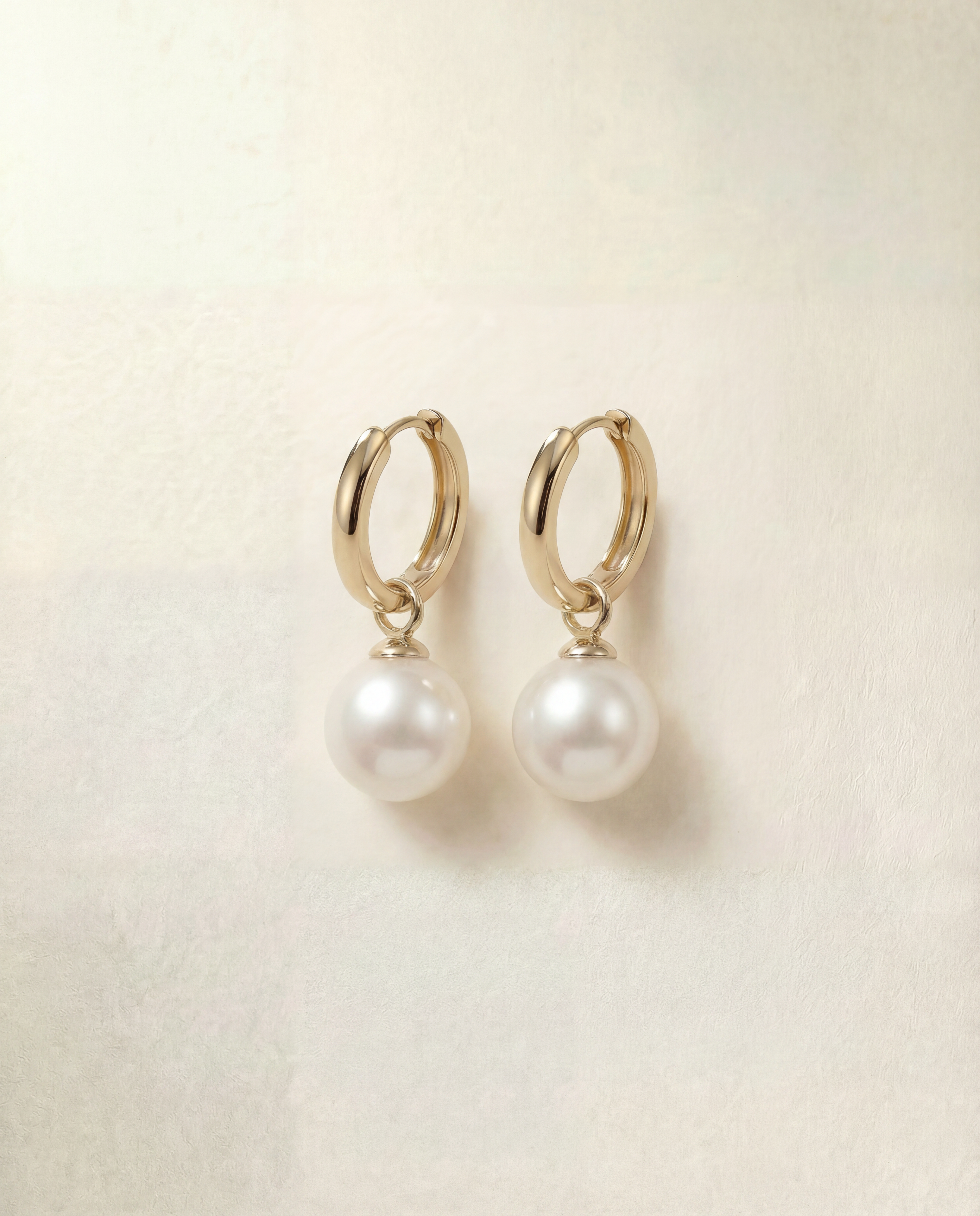 Pair of pearl earrings with gold hooks on a beige background