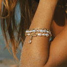 Close-up on arm wearing multiple South Sea keshi pearl and gemstone bracelets with diamond cushion cut charm.