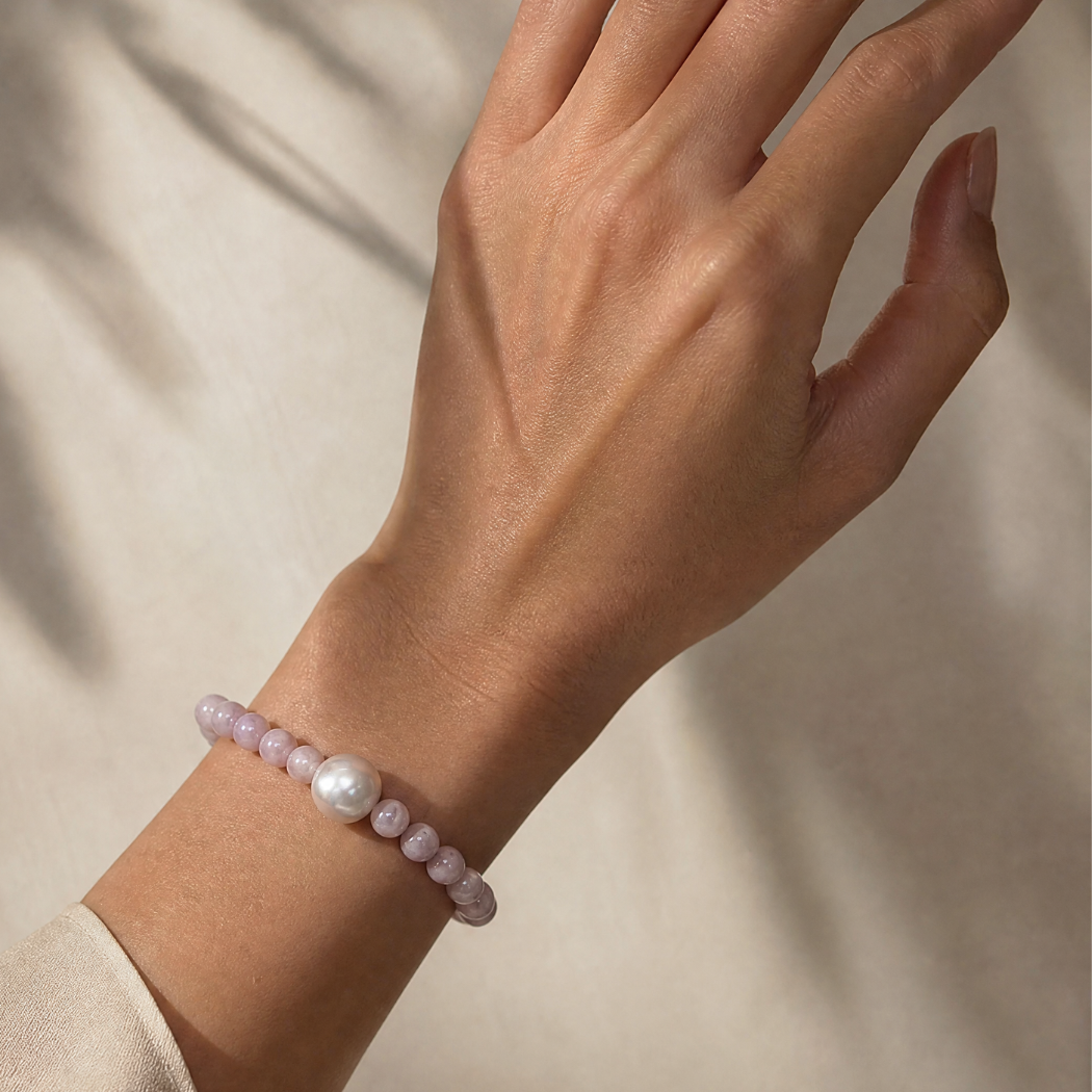 Hand wearing a bracelet with pink beads and a pearl on a neutral background