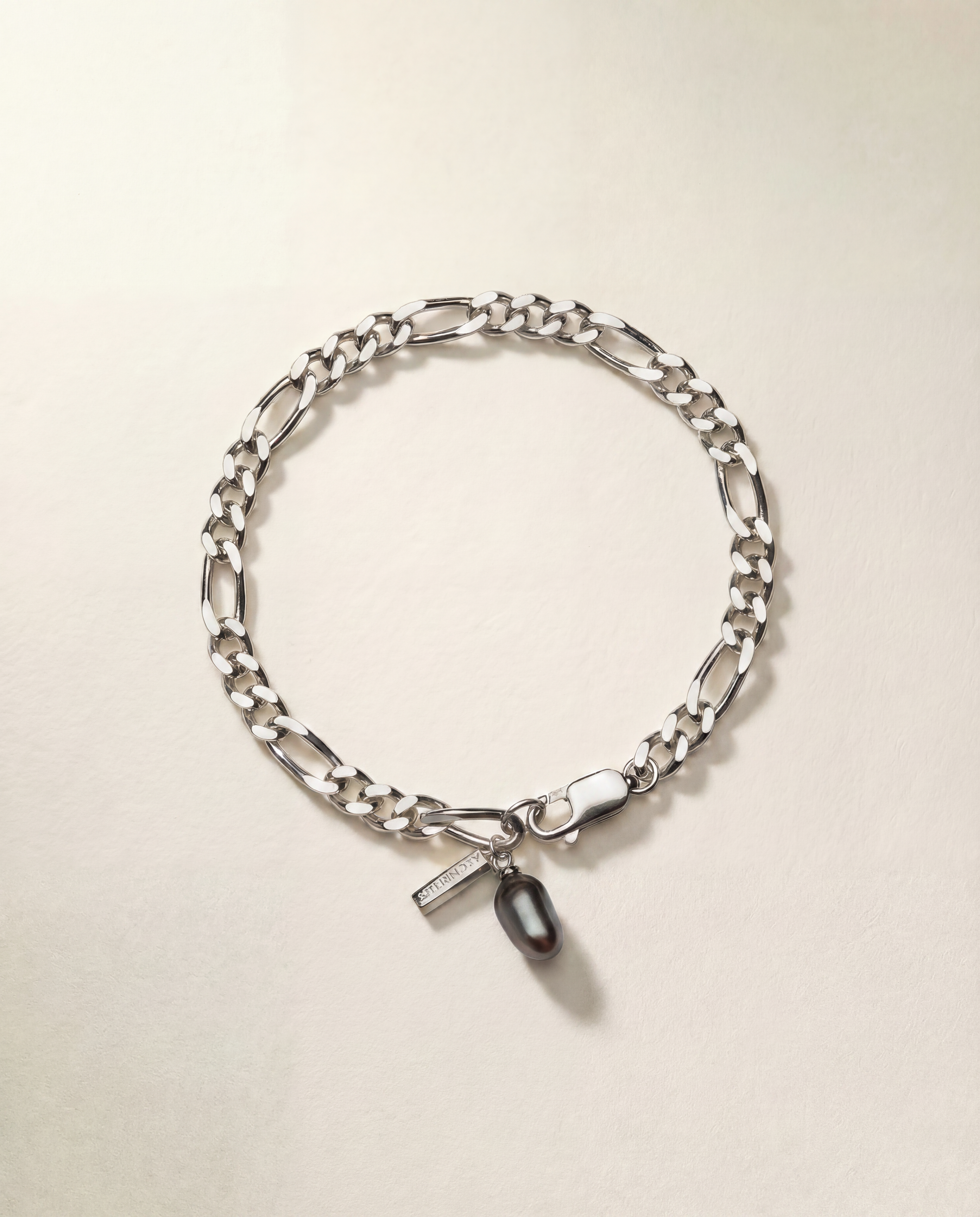 Silver chain bracelet with a tag and black pearl on a beige background