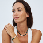 Woman wearing a malachite and gold beaded necklace and bracelet on a white background