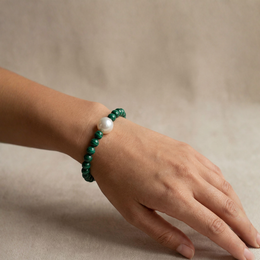 Hand wearing a green beaded bracelet with a pearl on a beige background