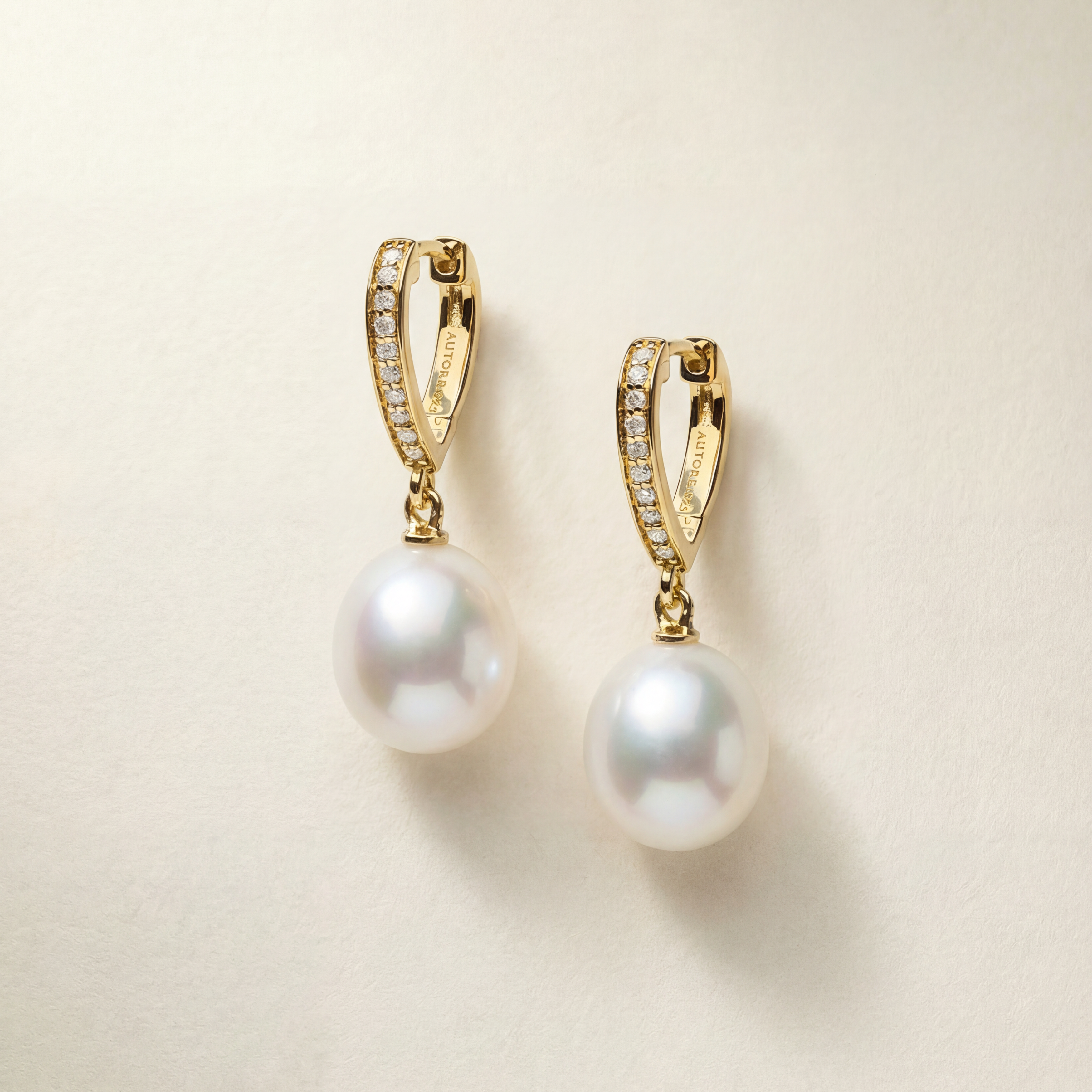 Gold earrings with pearl drops on a beige background