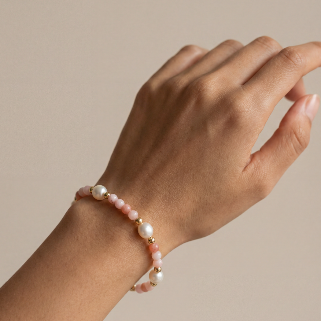 Hand wearing a pearl bracelet on a beige background