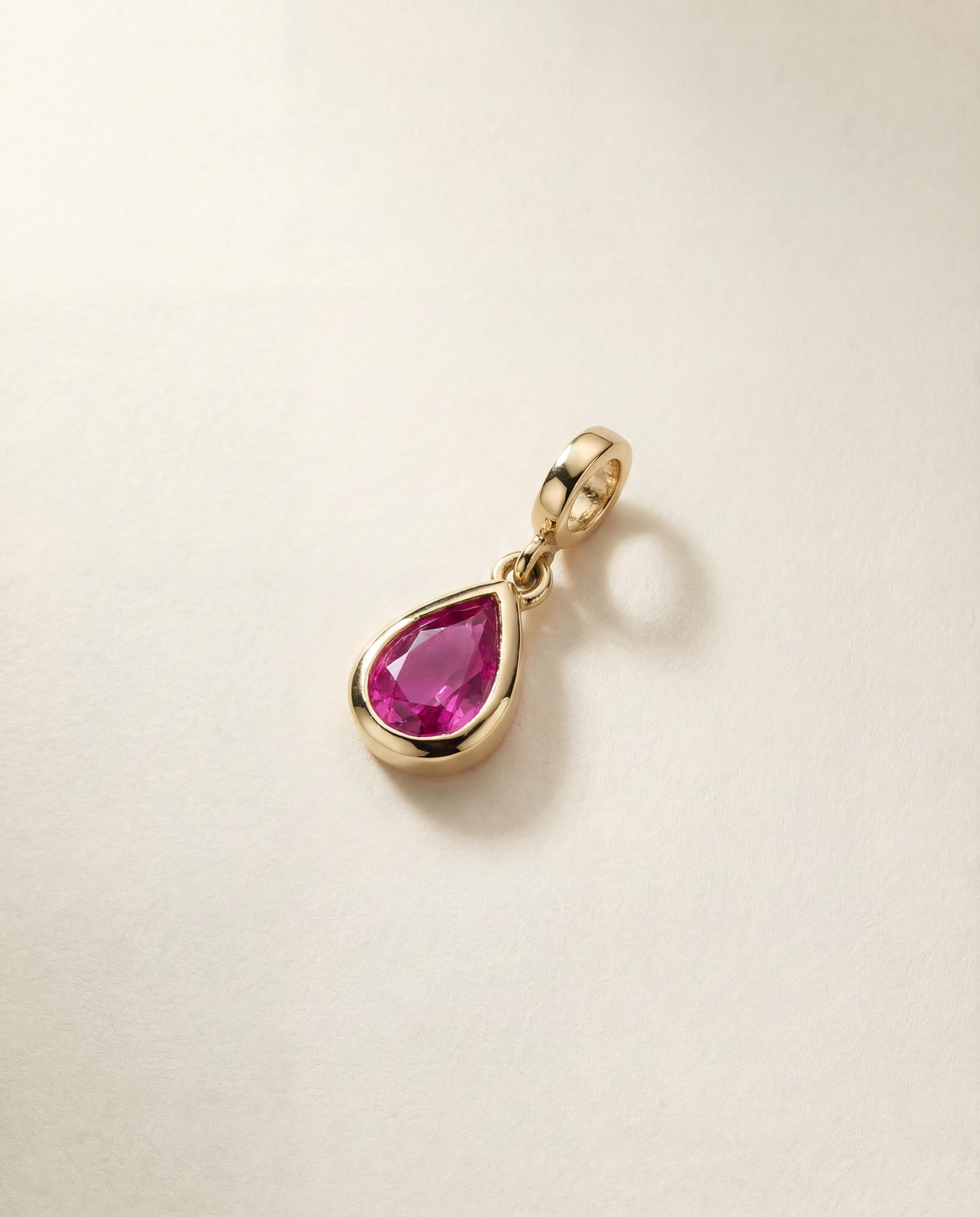 Gold charm with a pink sapphire gemstone on a beige background