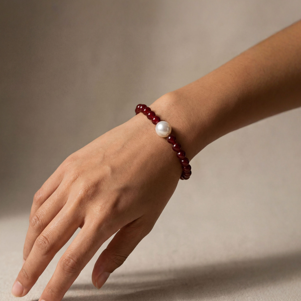Hand wearing a bracelet with a pearl bead on a neutral background