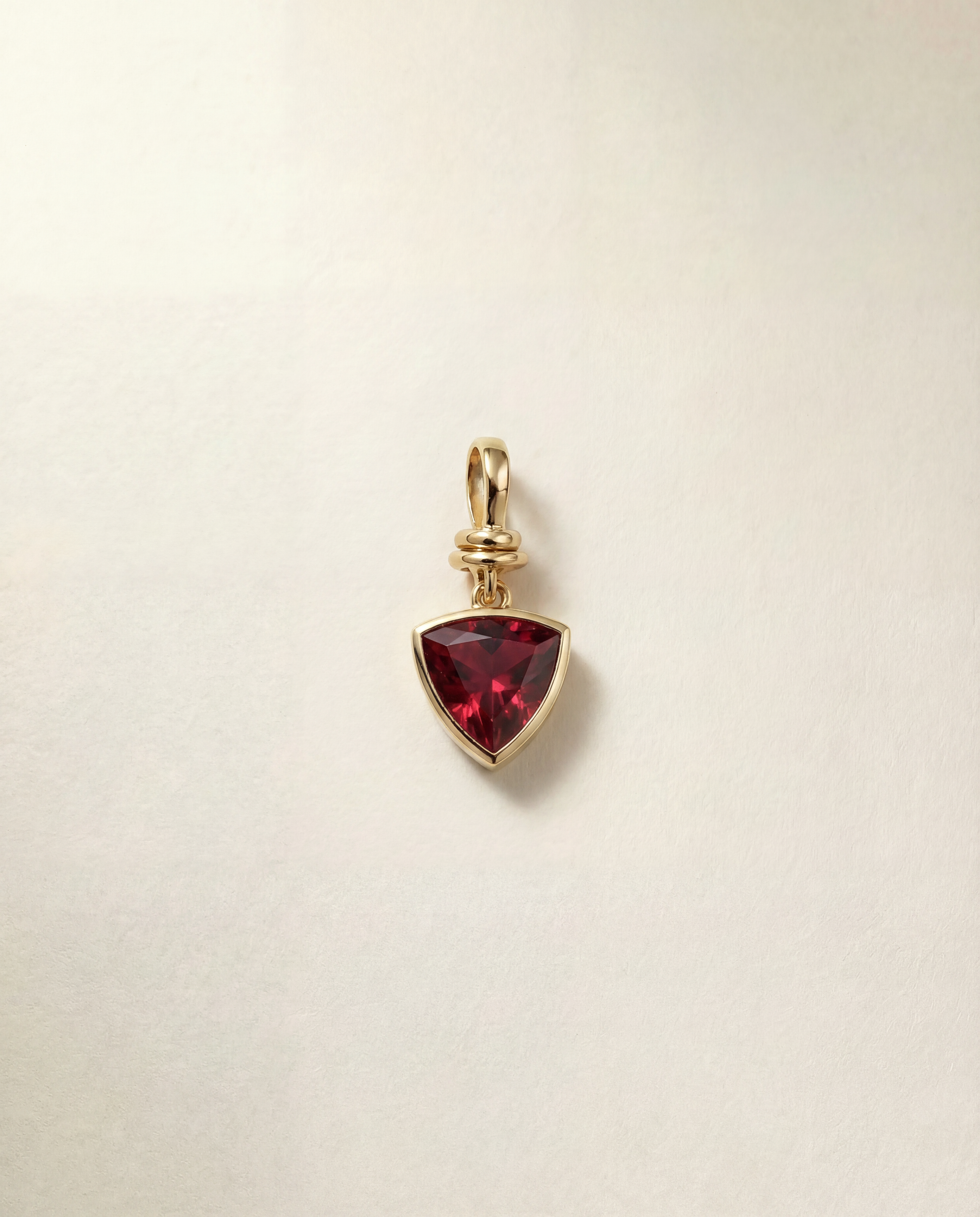 Gold pendant with a red gemstone on a beige background