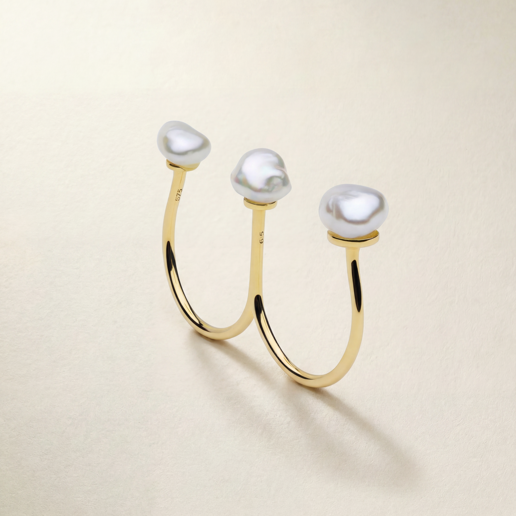 Gold ring with three pearls on a beige background