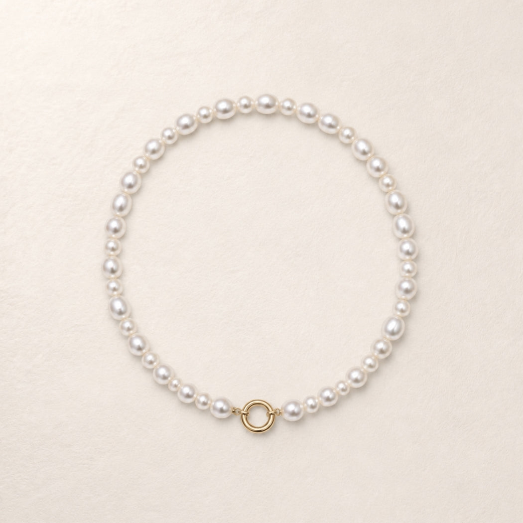 A classic south sea pearl necklace with a small gold ring clasp, displayed on a textured cream background.