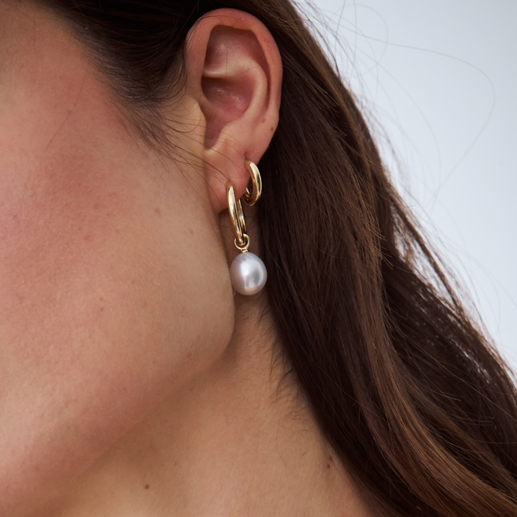 Close-up of an ear wearing a gold hoop earring with a south sea pearl charm.