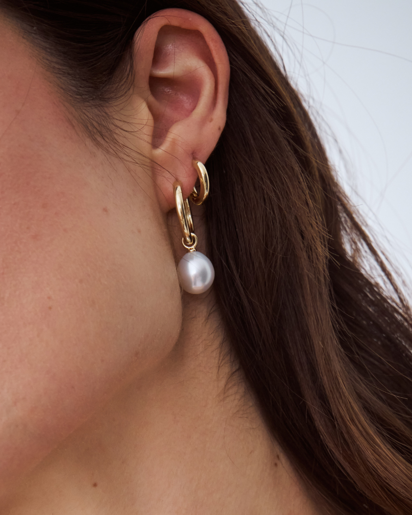 Close-up of an ear wearing a gold hoop earring with a south sea pearl charm.
