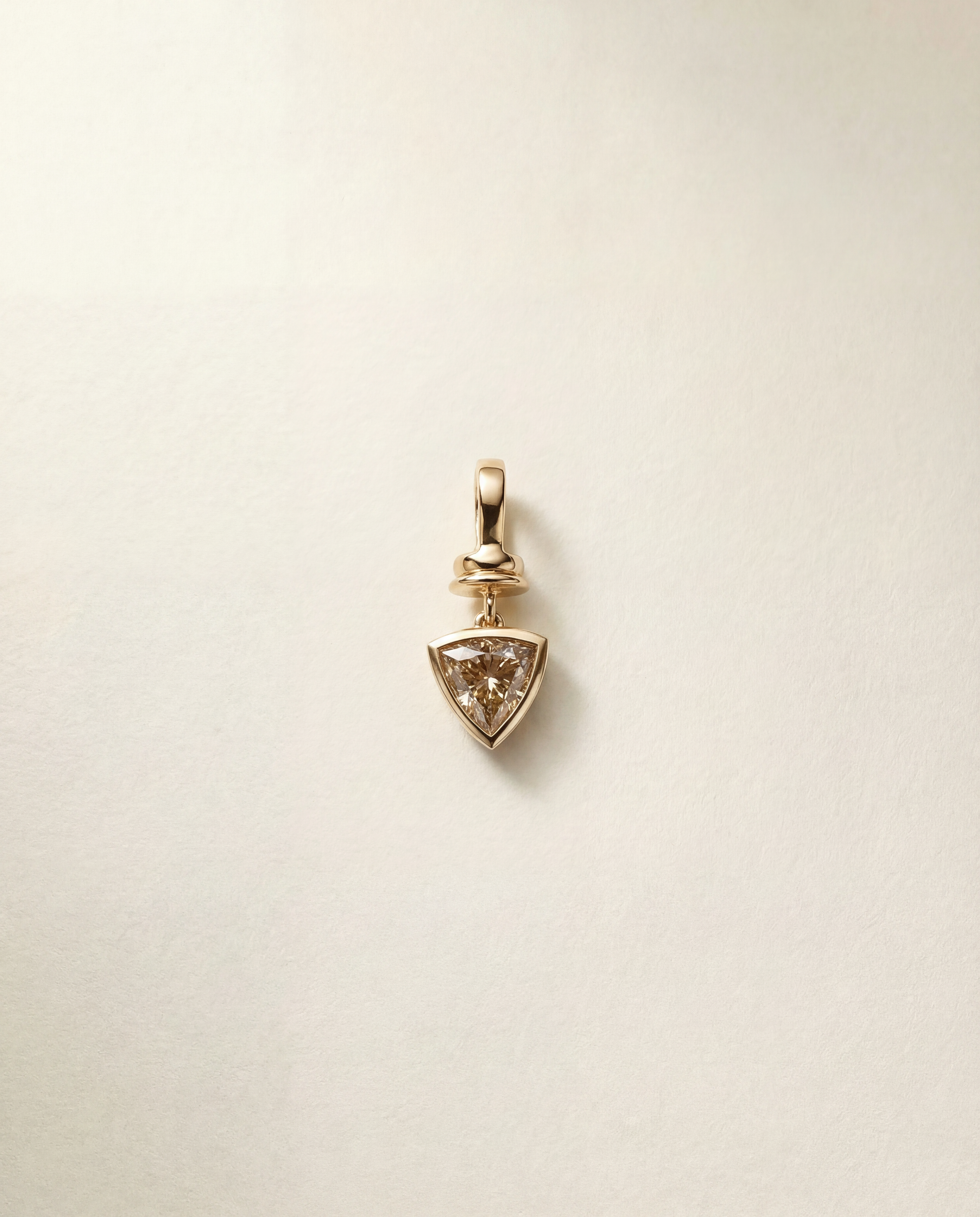 Gold pendant charm with a triangular champagne diamond on a beige background