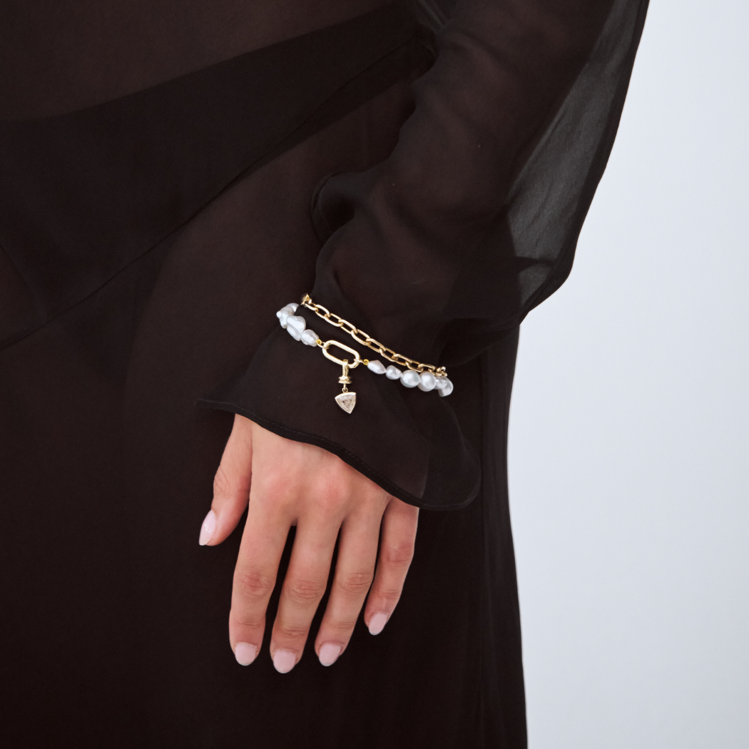 Model wearing a south sea keshi pearl bracelet with a trilliant champagne diamond charm. Stacked with a solid gold paperclip bacelet.