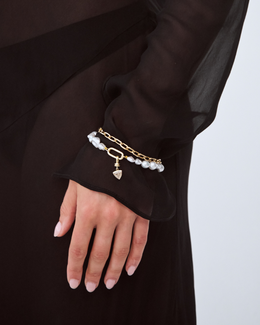 Model wearing a south sea keshi pearl bracelet with a trilliant champagne diamond charm. Stacked with a solid gold paperclip bacelet.