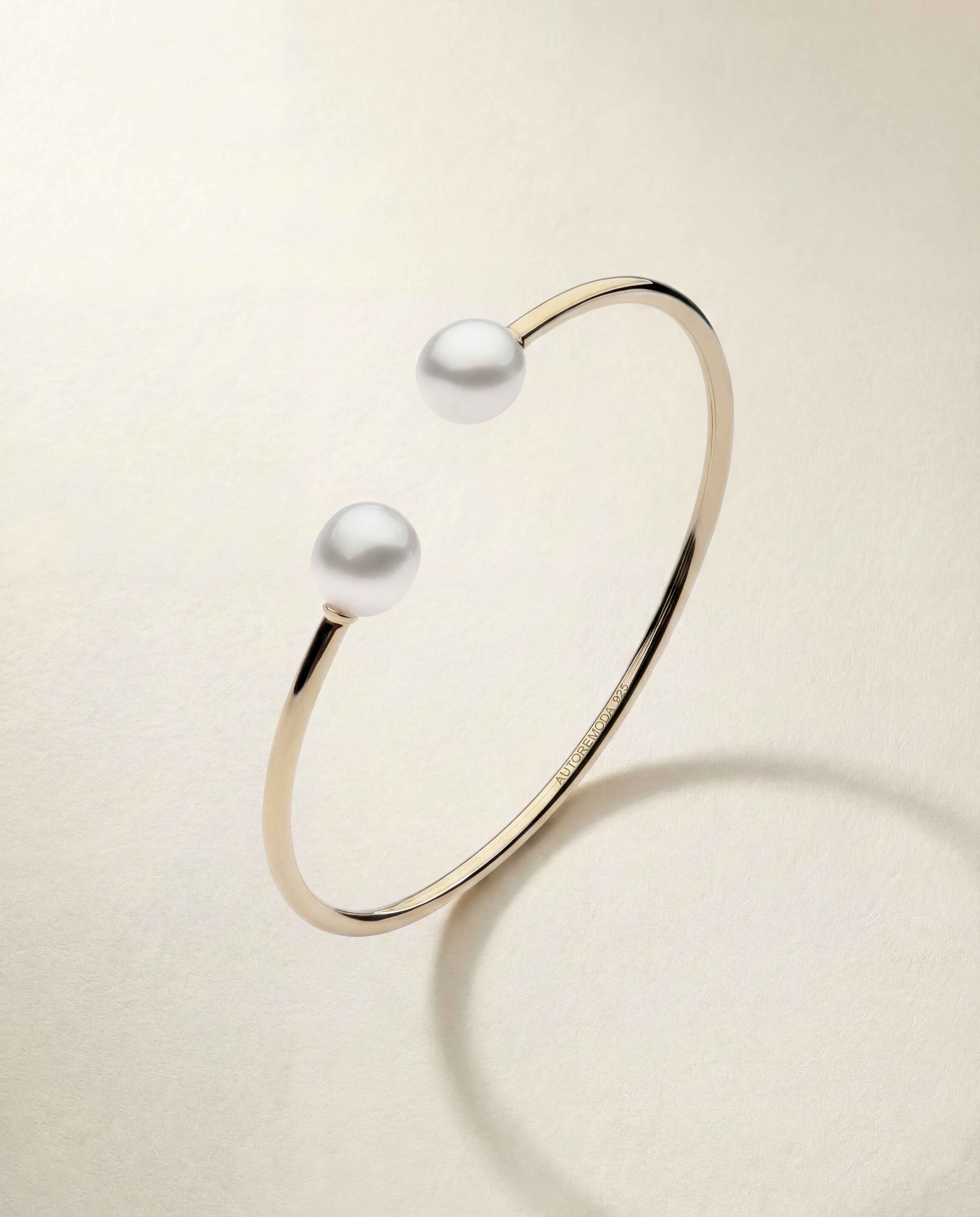 Gold bracelet with two pearls on a beige background
