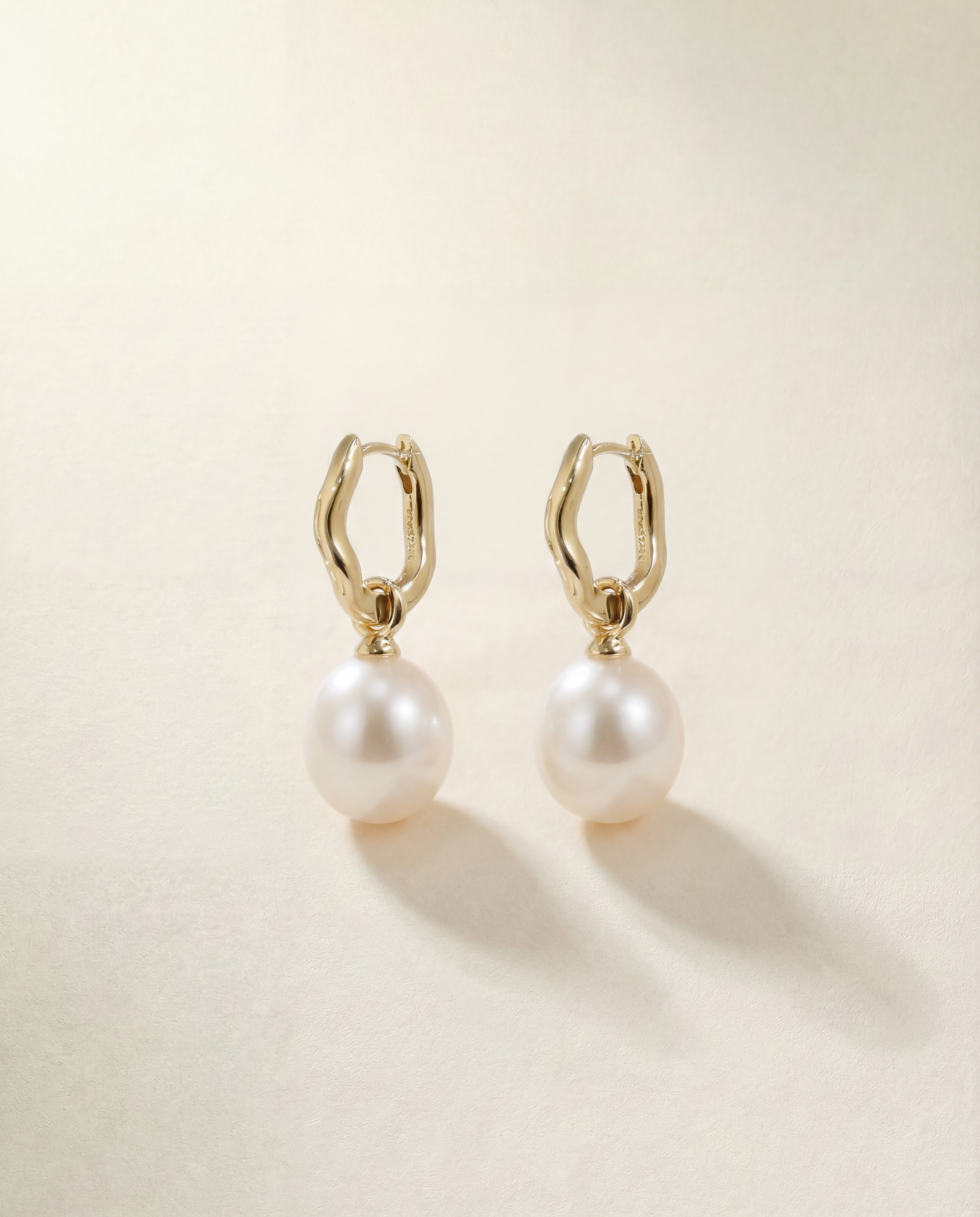 Pair of pearl earrings with gold hoop clasps on a beige background