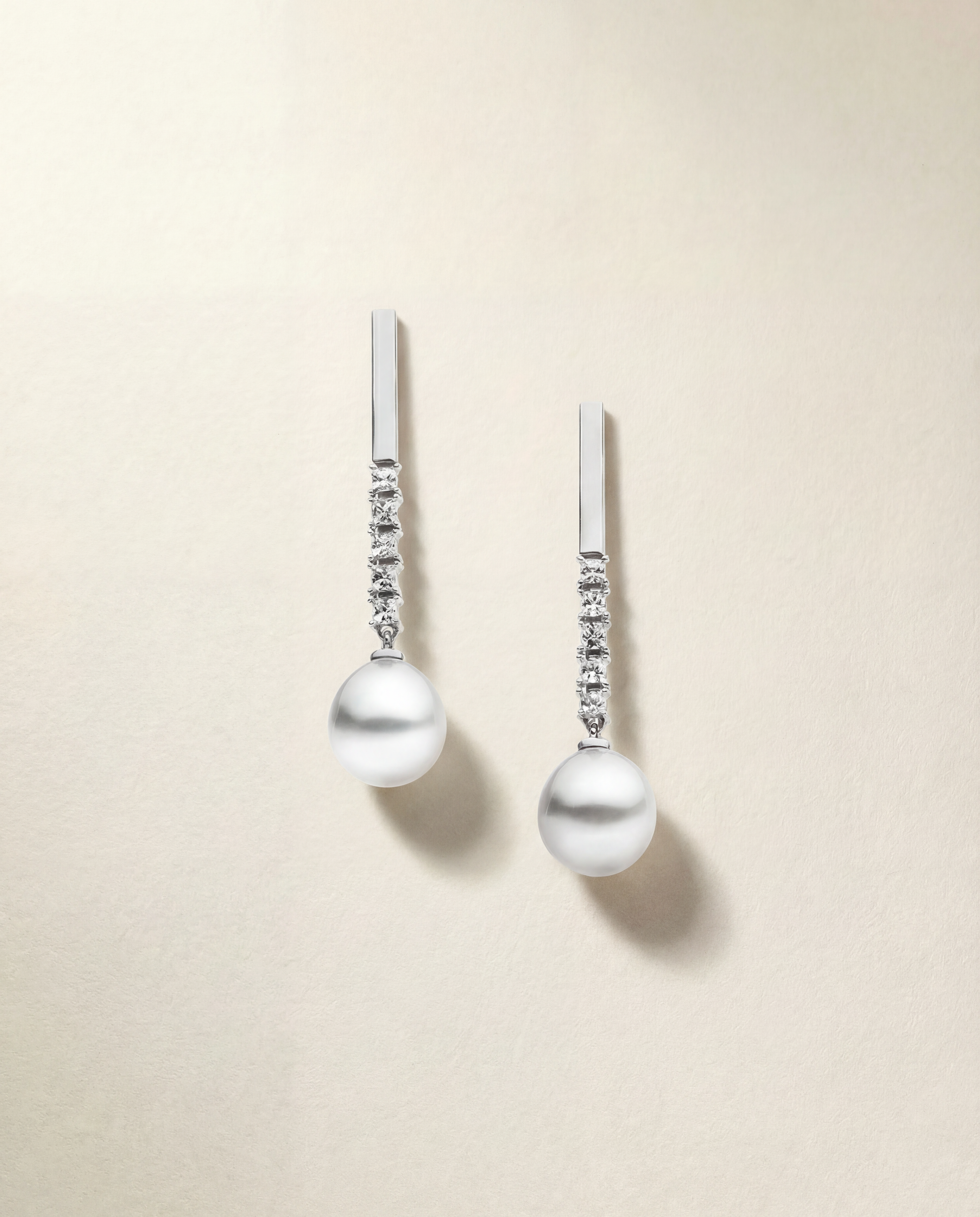 Pair of pearl earrings with white sapphire accents on a beige background