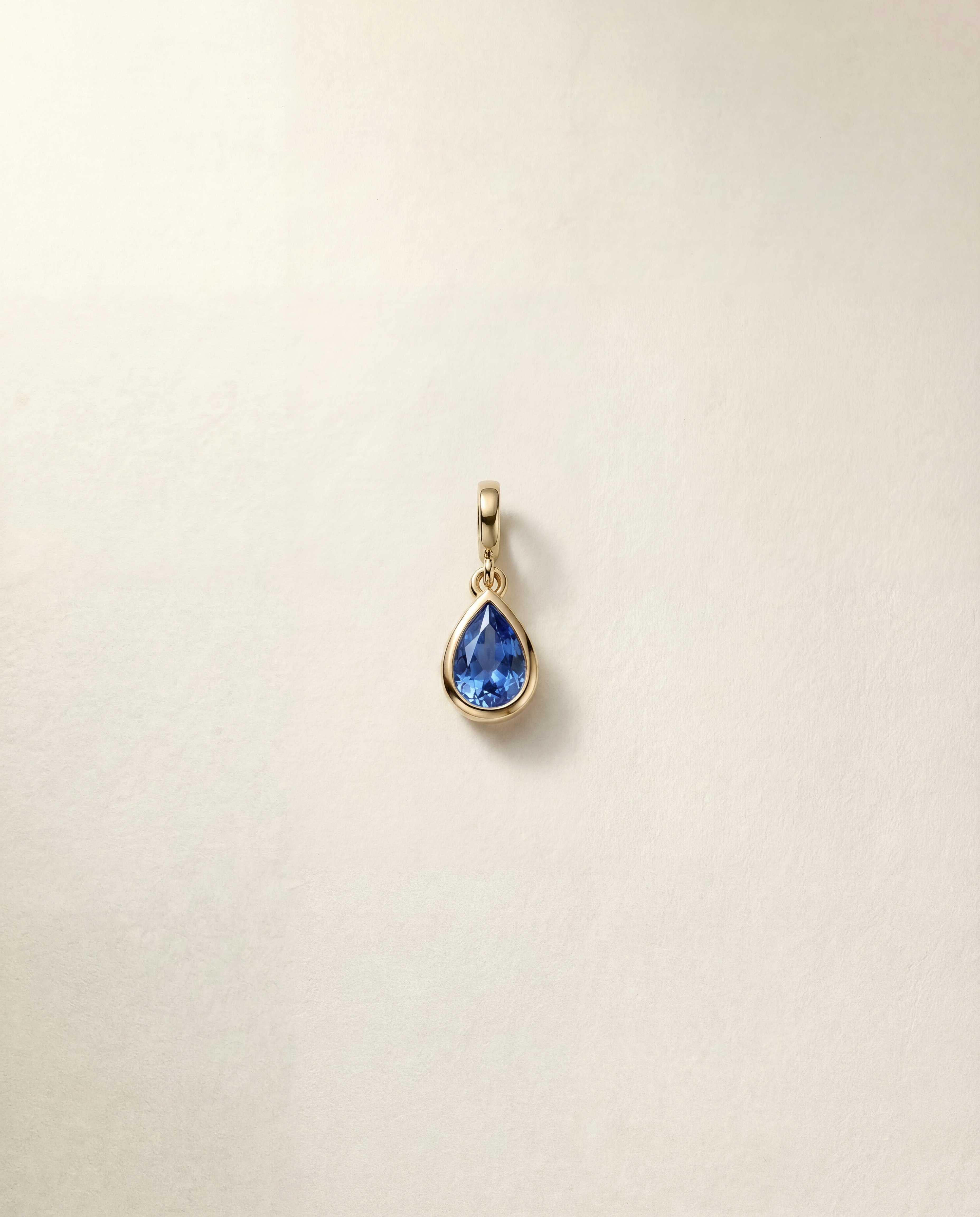 Gold pendant with a blue gemstone on a beige background