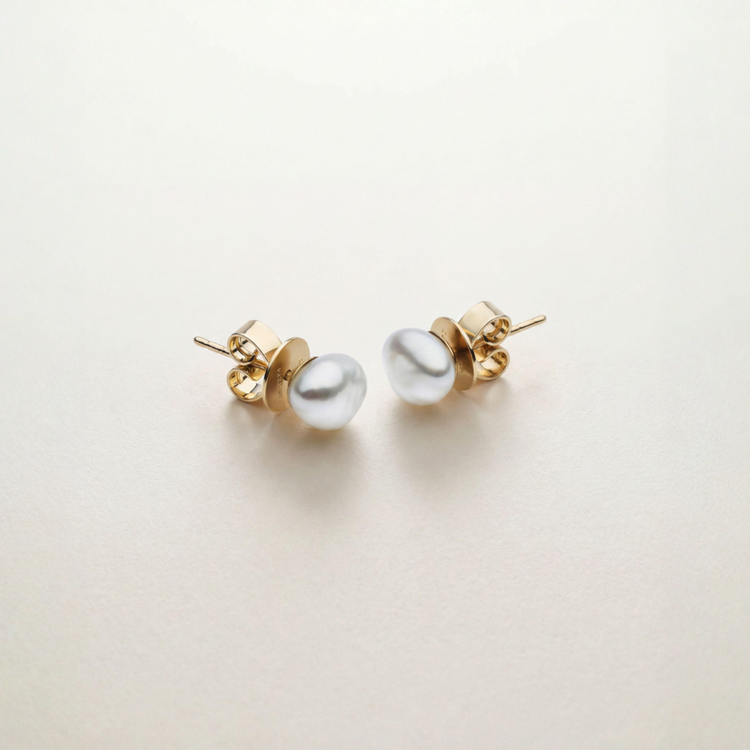 Pair of pearl earrings with gold settings on a light beige background