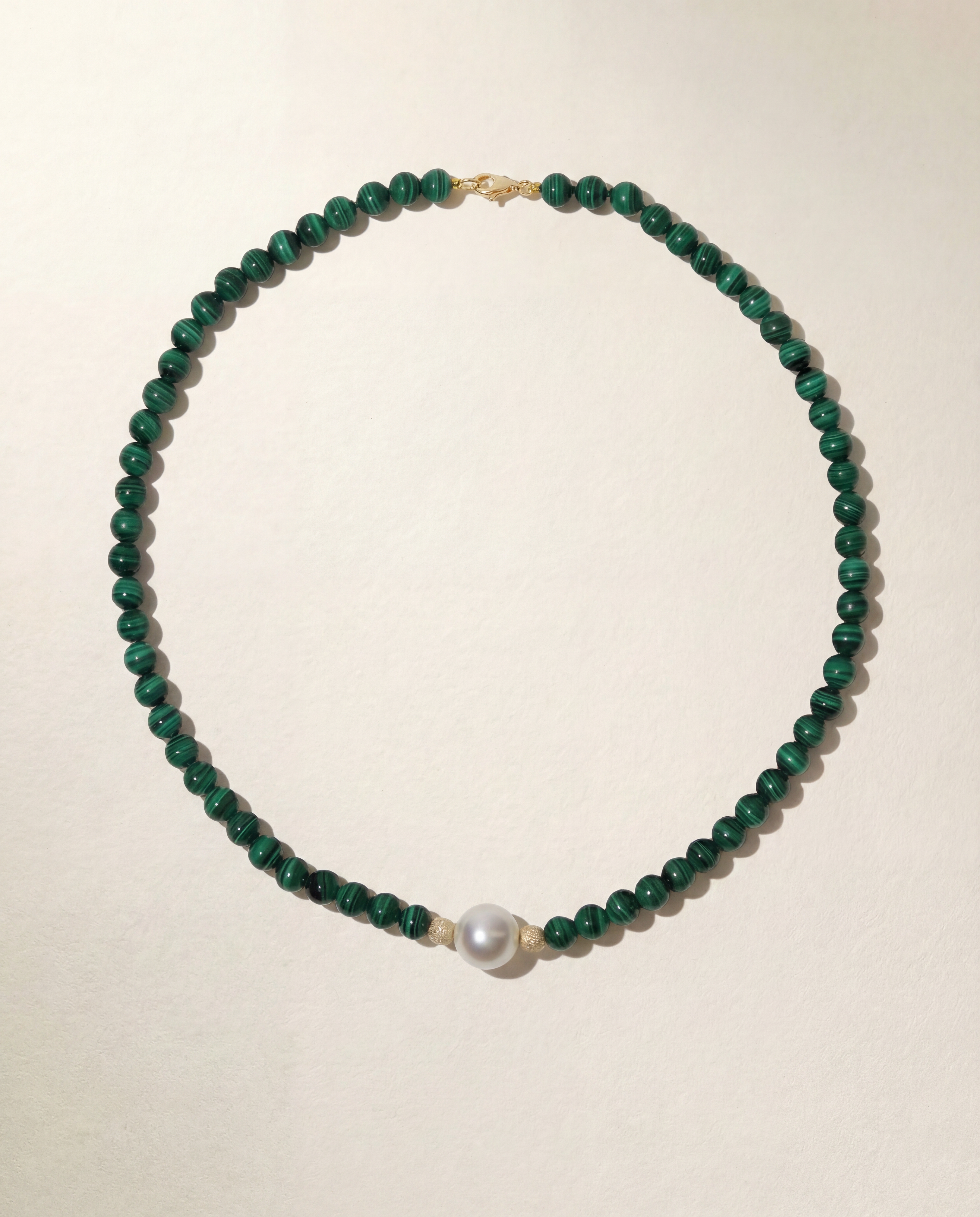Necklace with green beads and a pearl on a beige background