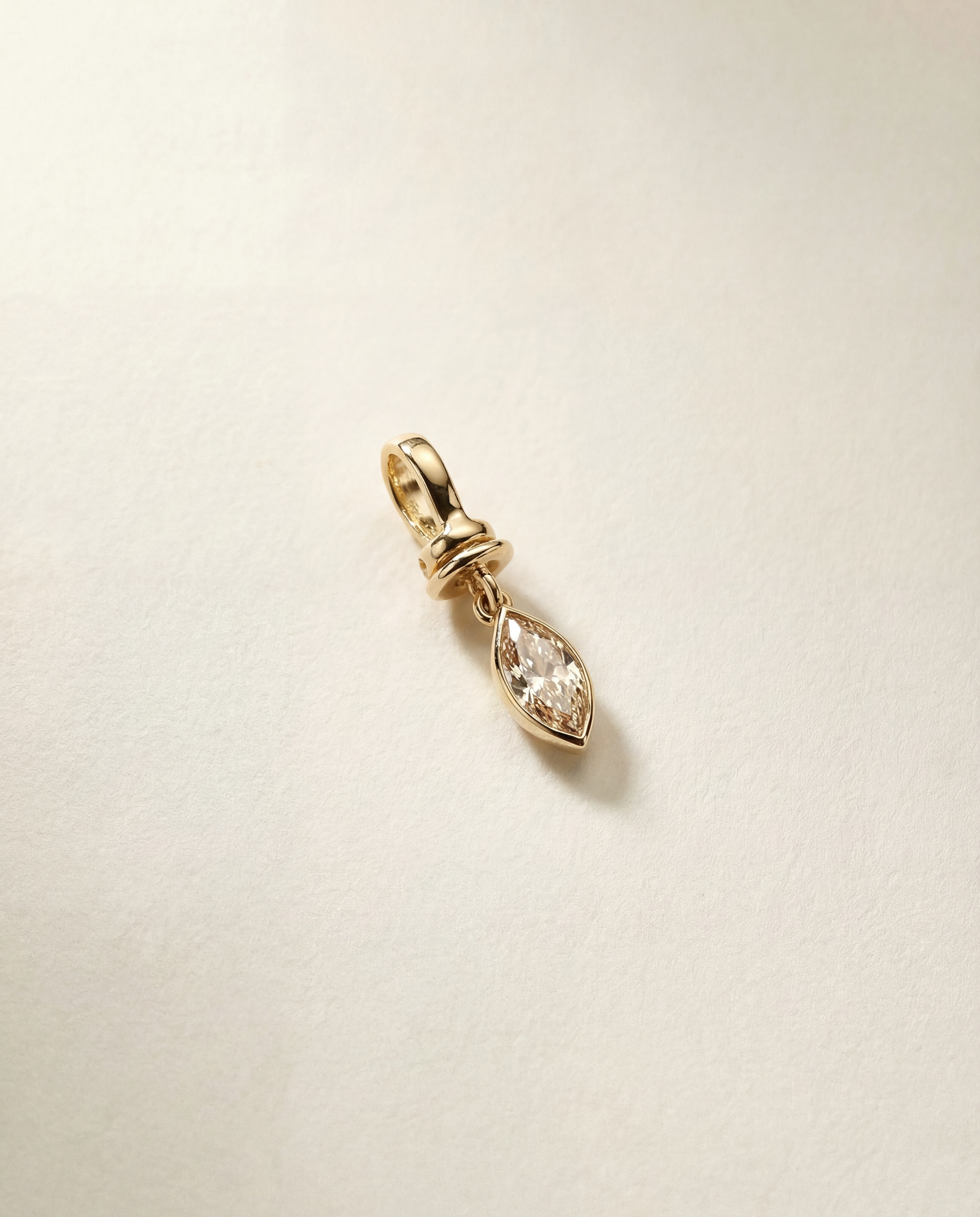Gold pendant with a champagne diamond on a light beige background