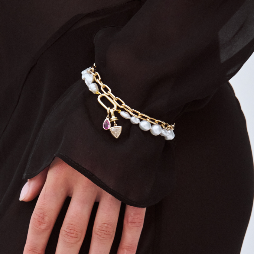 model wearing a south sea keshi pearl bracelet with a pink sapphire charm. Stacked with a champagne diamond charm and paperclip chain bracelet