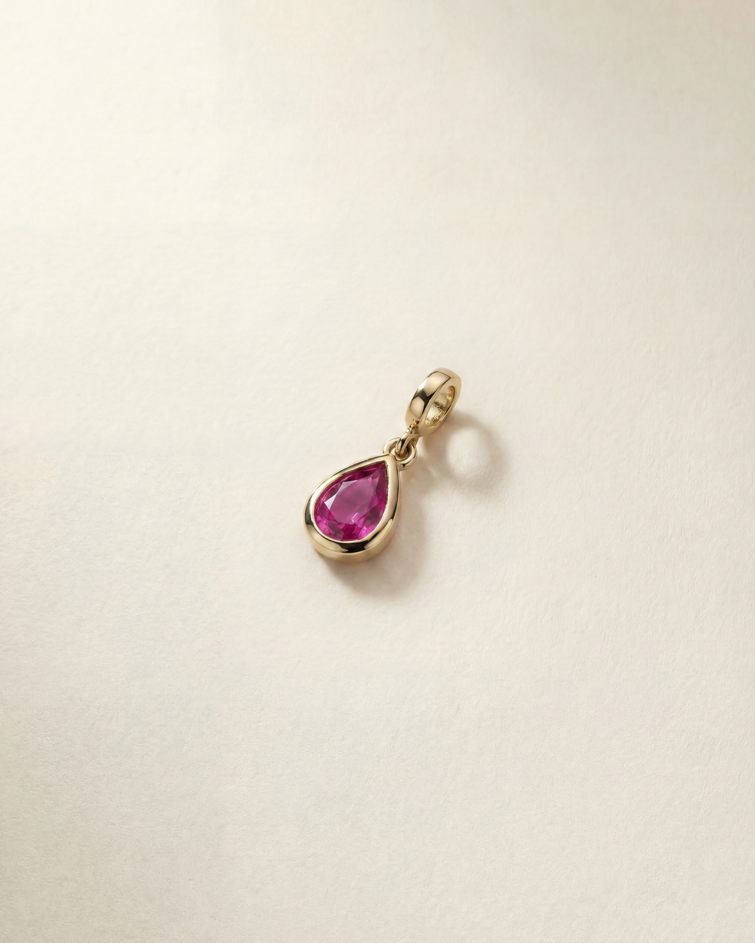 Gold charm with a pink gemstone on a beige background