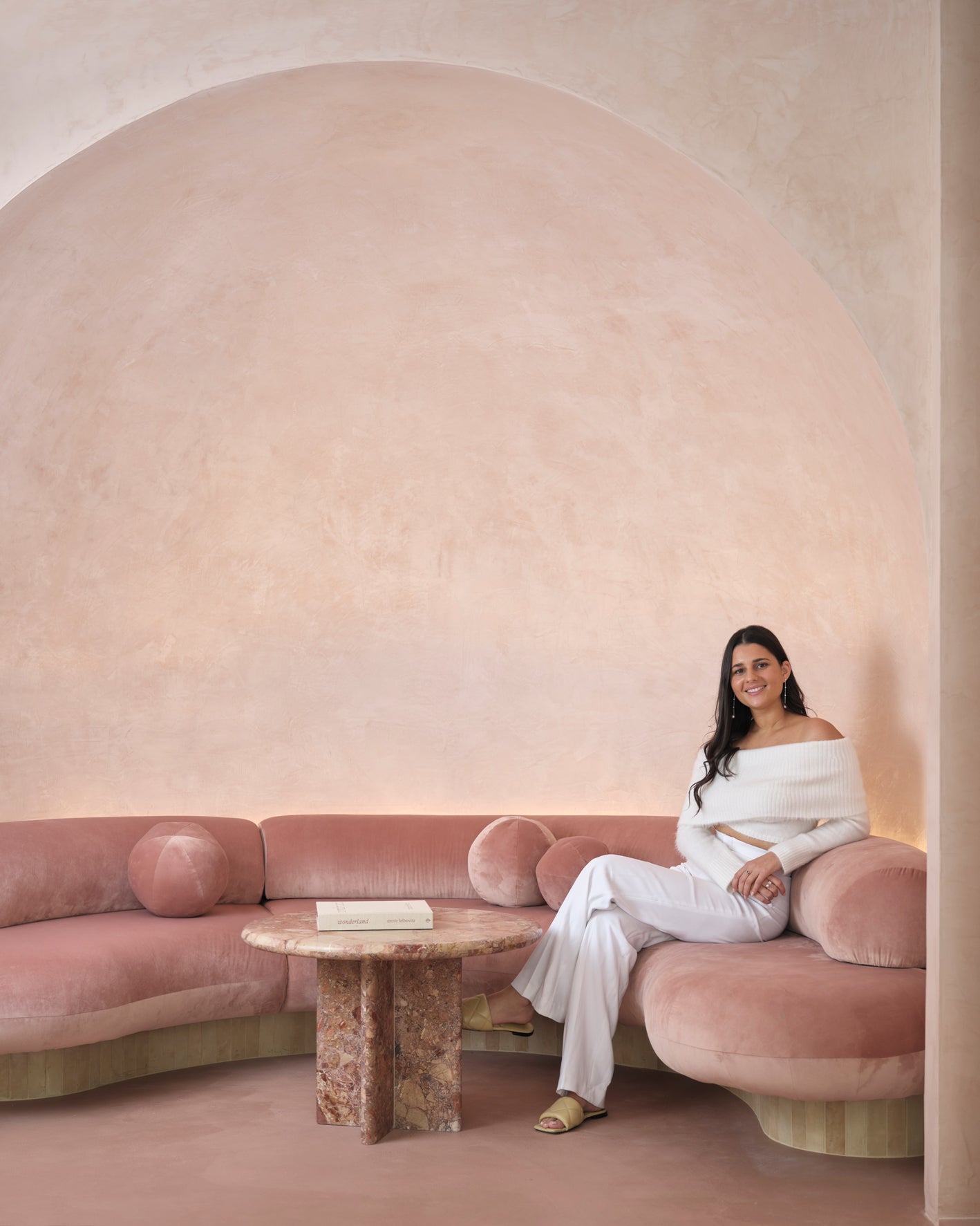 Woman sitting on a pink sofa in a room with a curved wall.