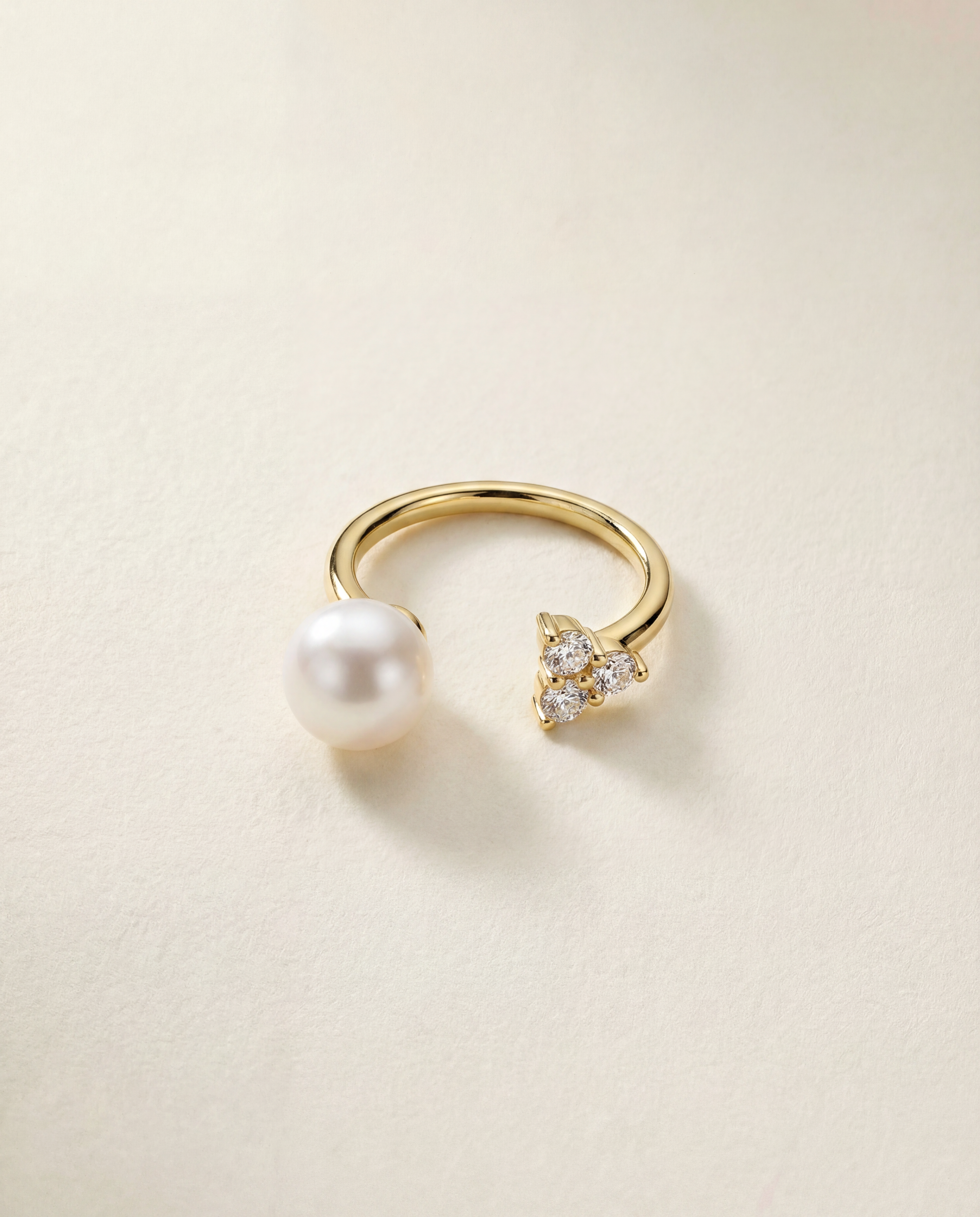 Gold ring with a pearl and small white sapphires on a beige background